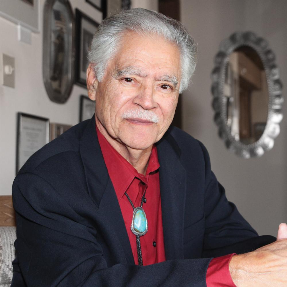 Portrait of Rudolfo Anaya, wearing a red shirt, in his home