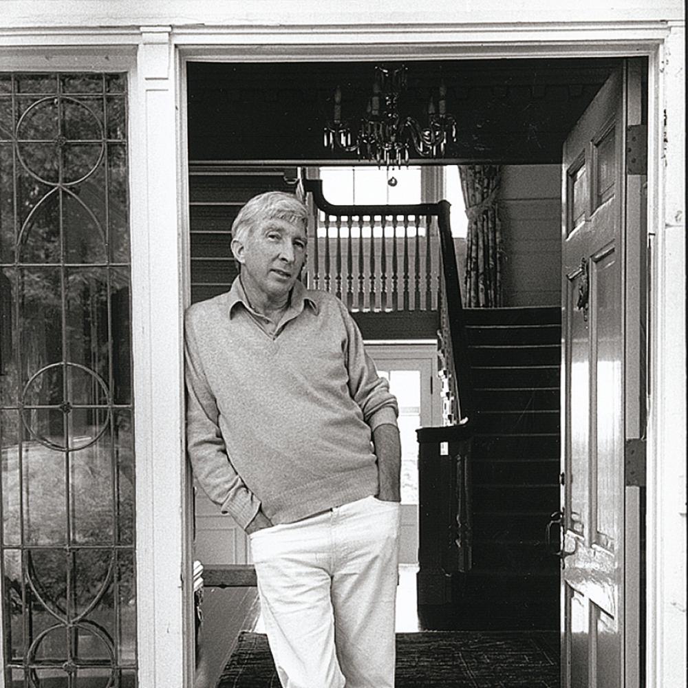Black and white photo of man leaning against doorway