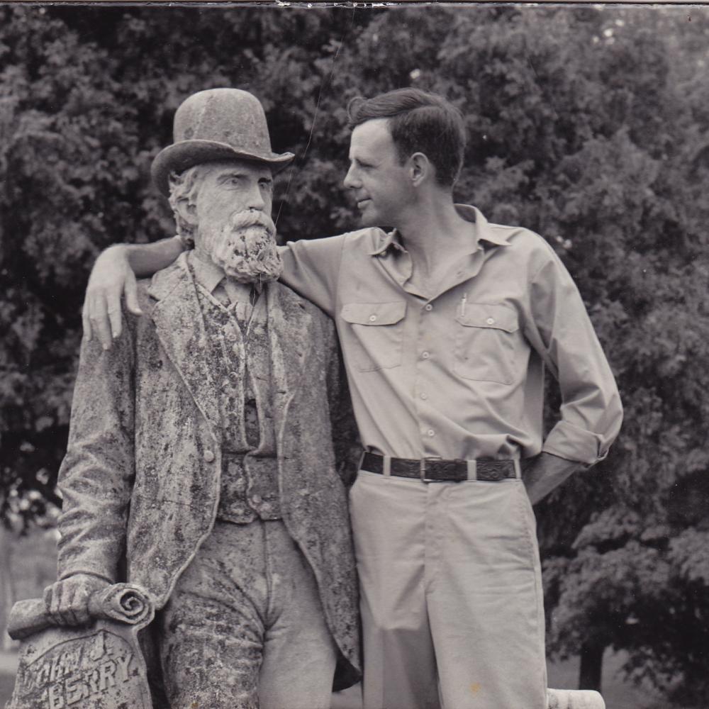 Black and white photo of Wendell Berry putting his arm around the statue of an old man.