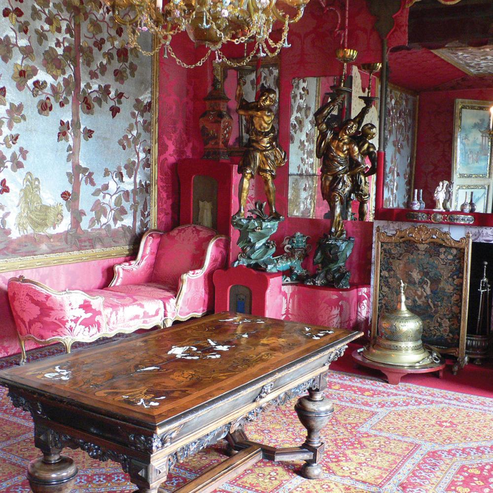 A room in Hauteville House, with bright pink walls, a large wooden table, and ornate, pink furniture