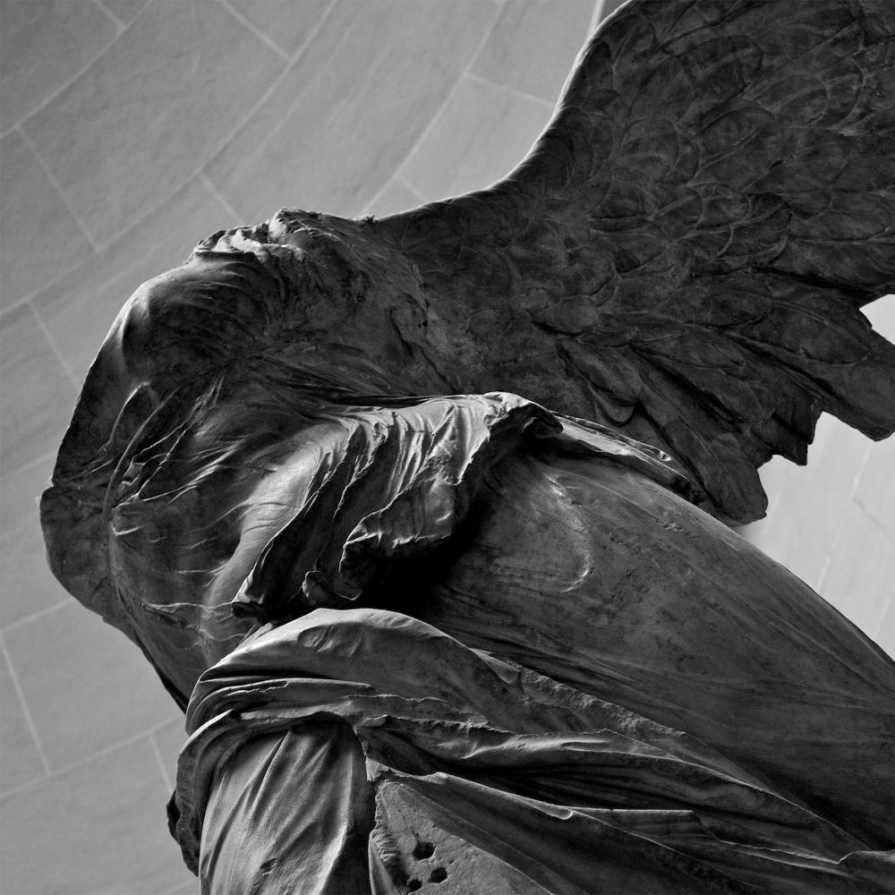 Black and white photo of a winged statue with no head.