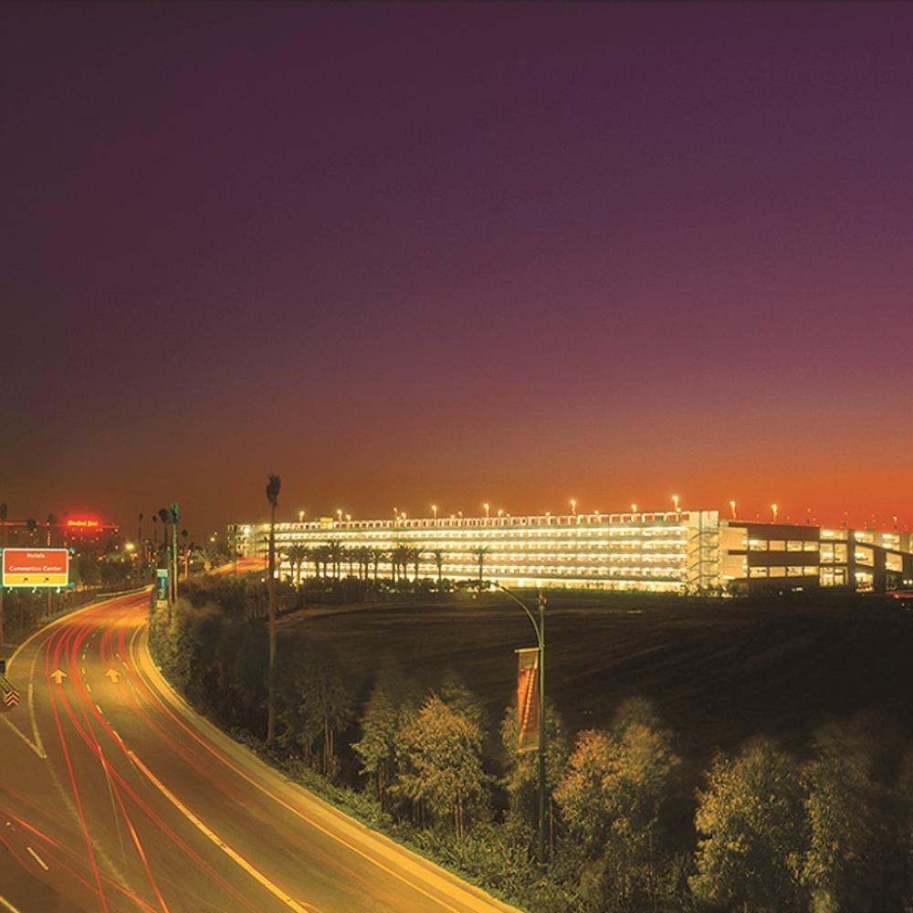 Photograph of a parking structure in distance, highway in foreground, at sunset