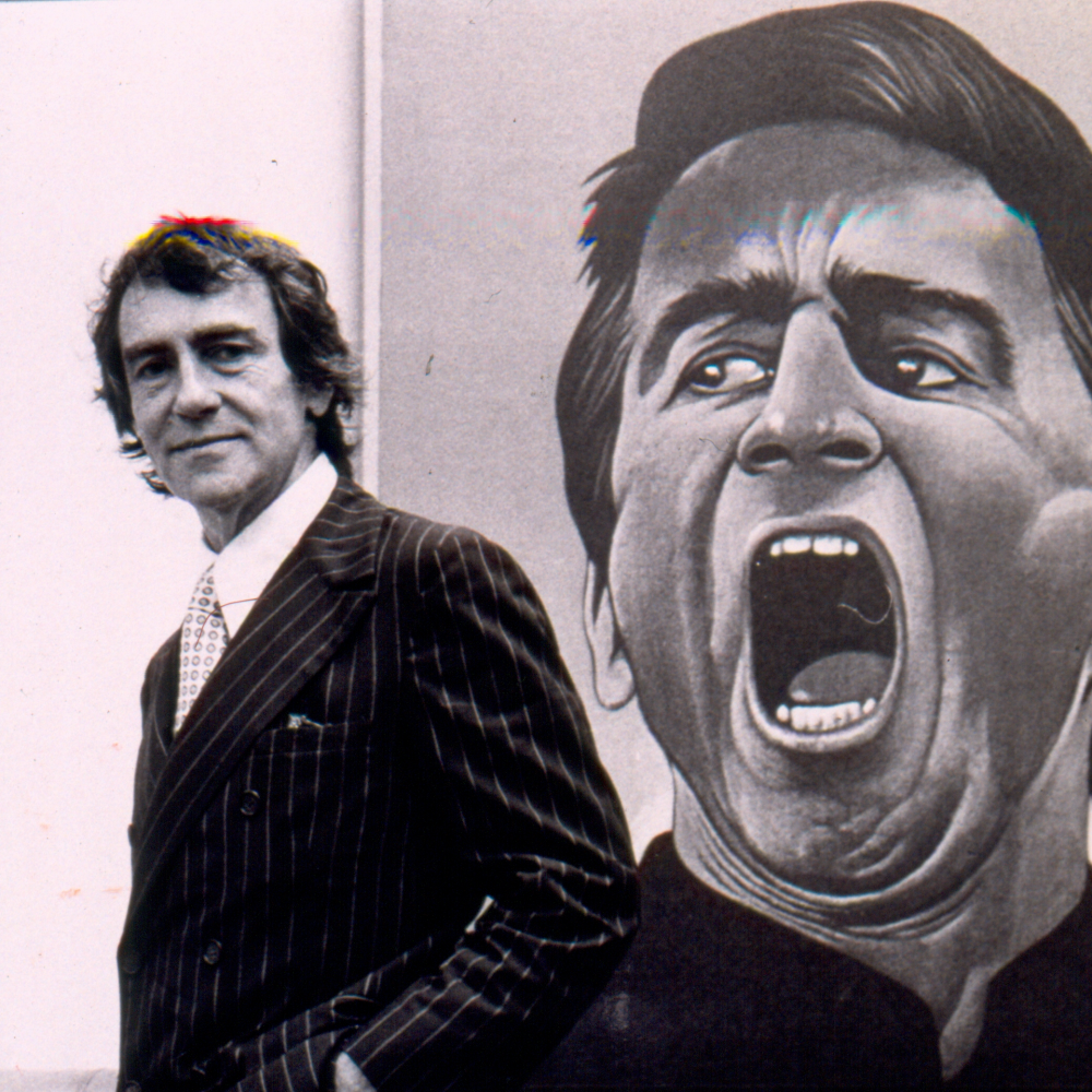 black and white photo of Joe Papp, left, standing next to a poster for Hamlet.