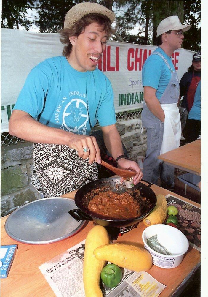 A man with a hat and t-shirt cooking a stew