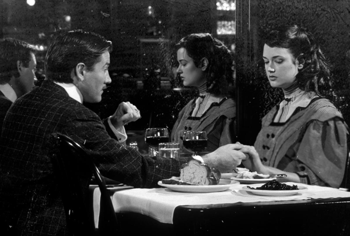 black and white film still of a man and woman holding hands across a table