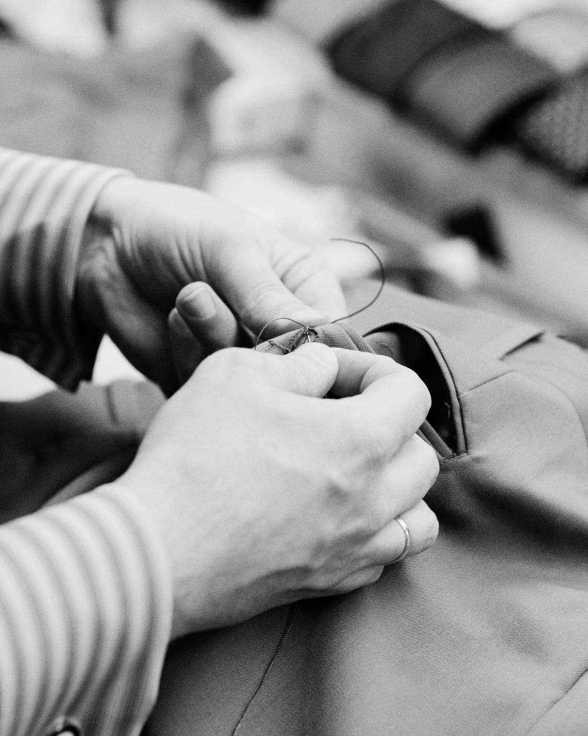 black and white photo of a pair of hands hand sewing stitches into a suit