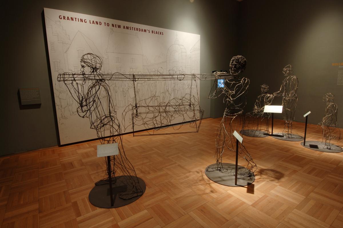 2 men sculpted out of wire, holding a beam between them