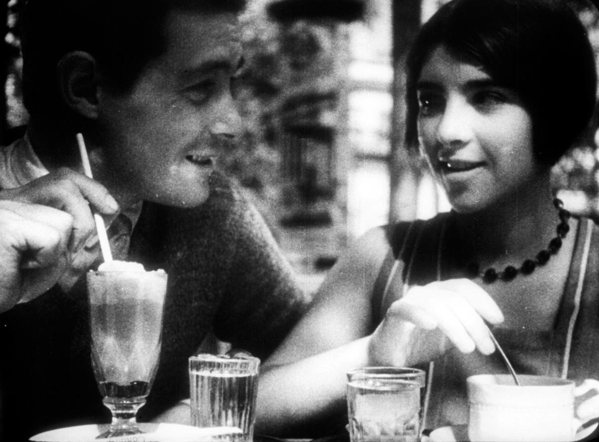 black and white film still of a man and a woman drinking out of glasses at a table