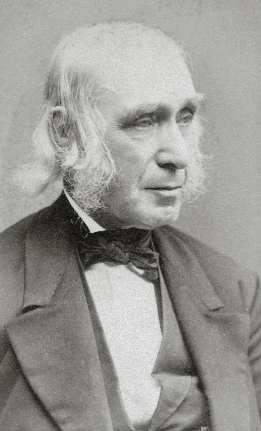 Alcott in a black suit and bow tie, facing slightly to his left