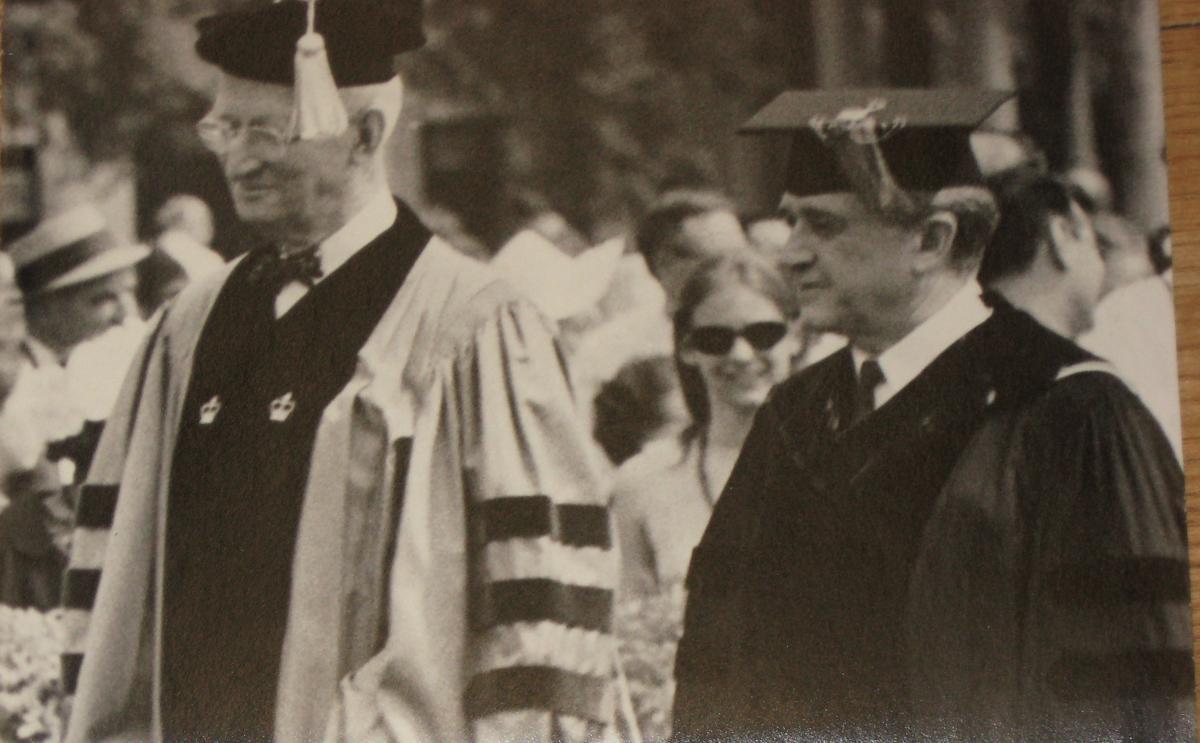 Mosely in dark collegiate robes and mortarboard cap, walks next to Robinson, who is in Columbia's blue and black robes and tasseled cap