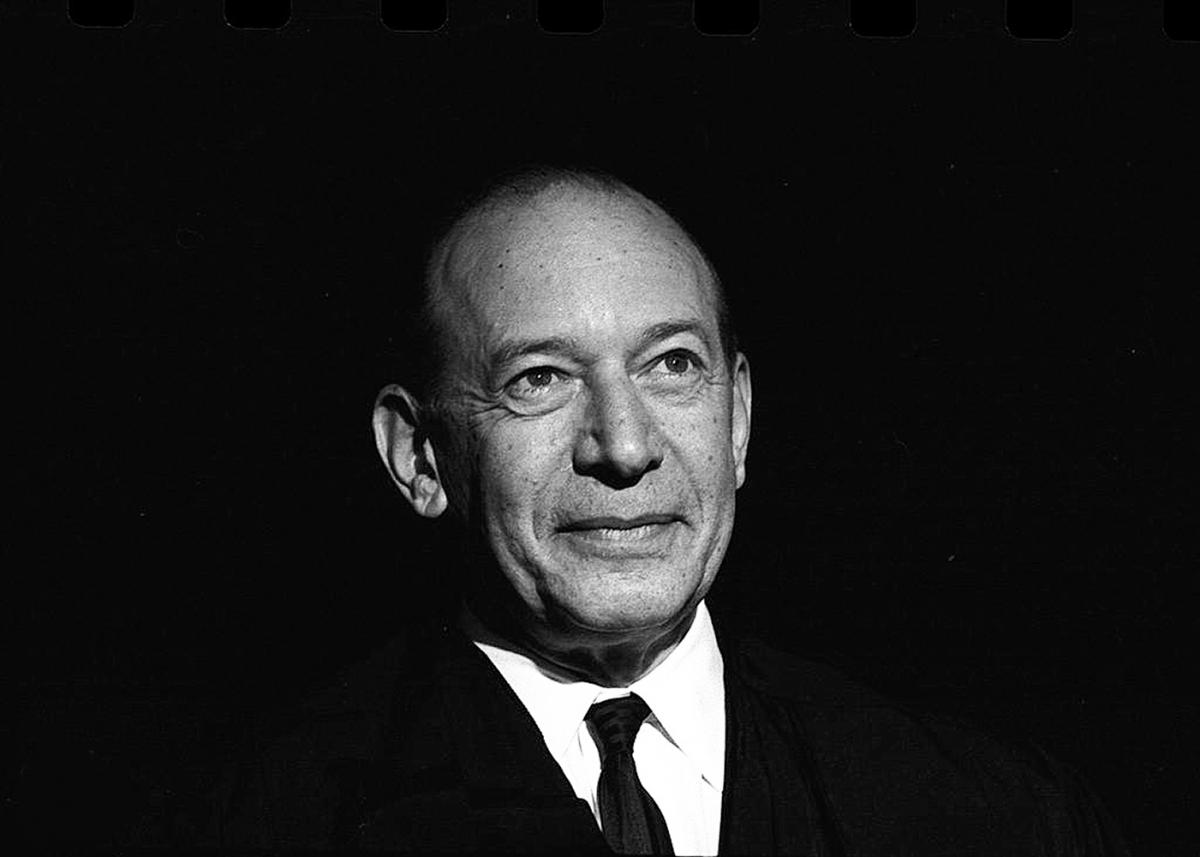 Black and white photo of Fortas, looking off into the distance, smiling slightly, wearing a dark suit and tie