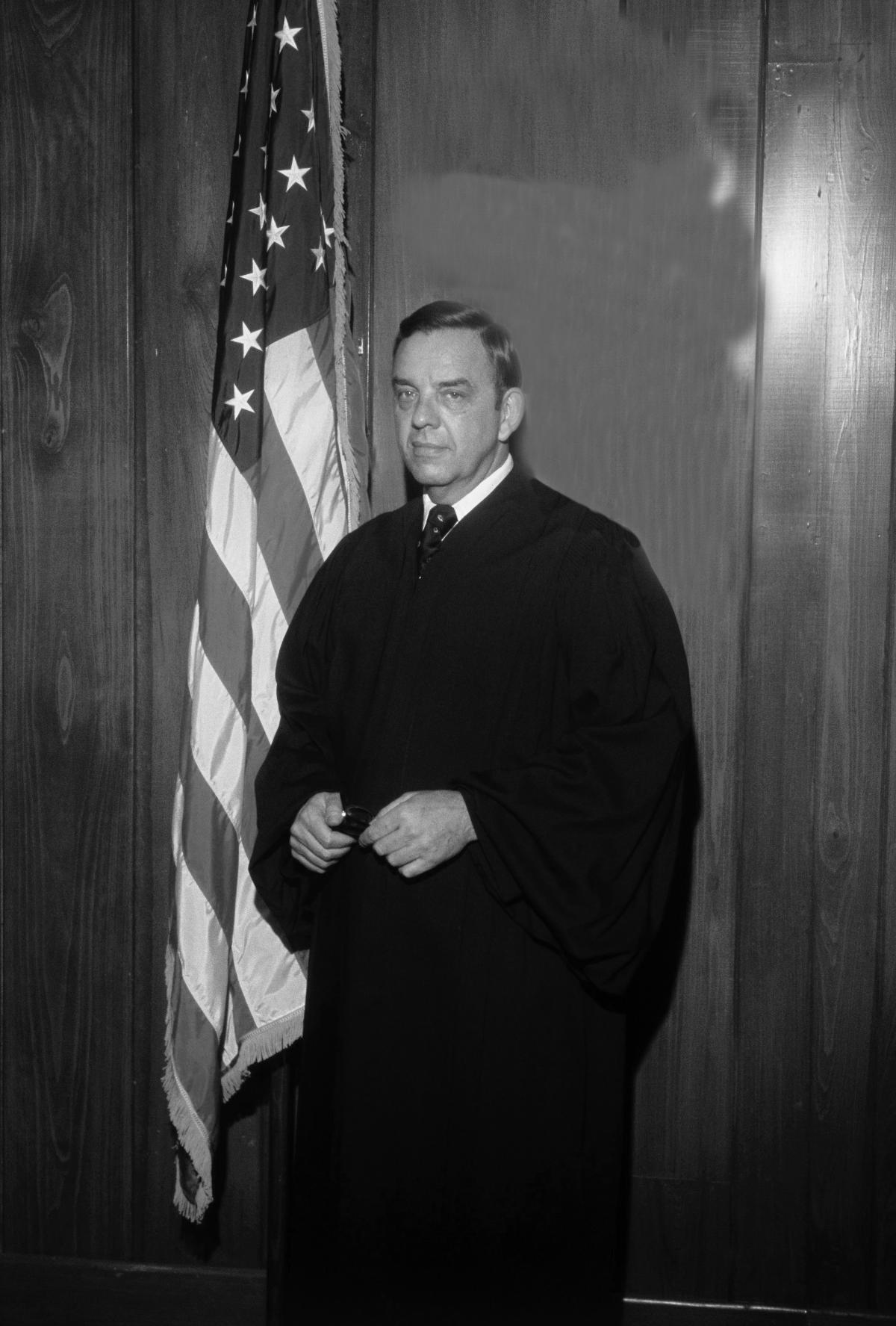 Carswell wearing judge's robes, standing in front of the American flag