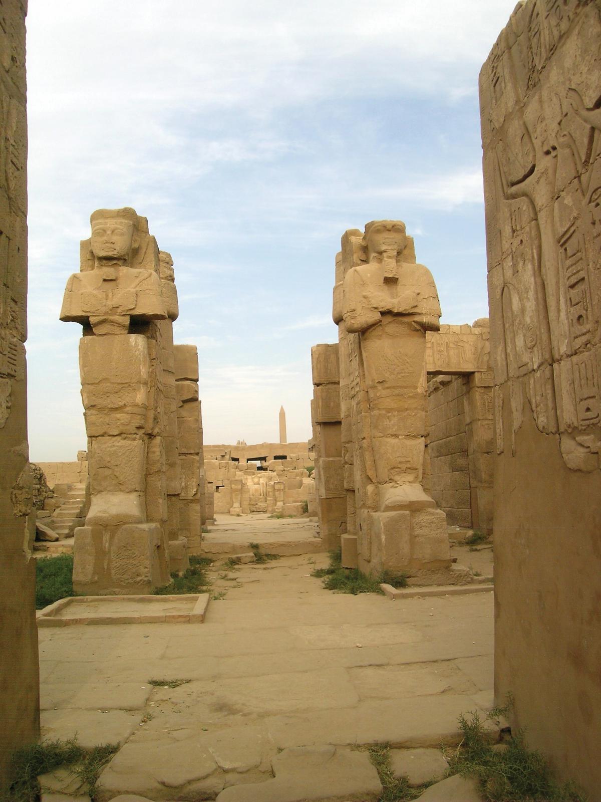 Huge sandstone statues of rulers and gods flank the entrance to a temple, also made of yellow sandstone