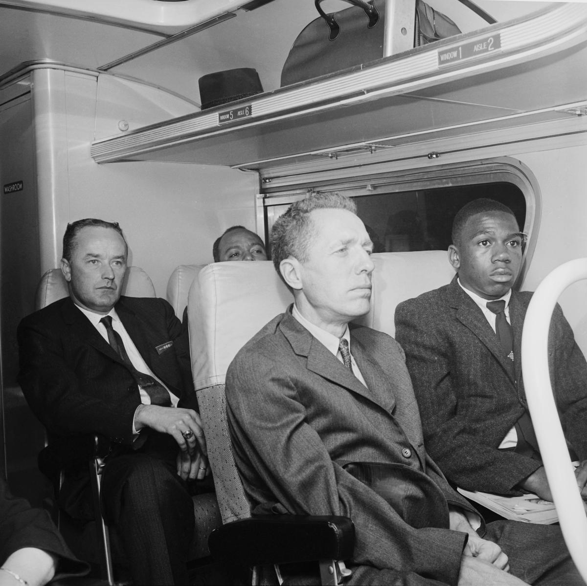 A white man and an African American man, in suits, sit next to each other on one of the Freedom Riders' buses