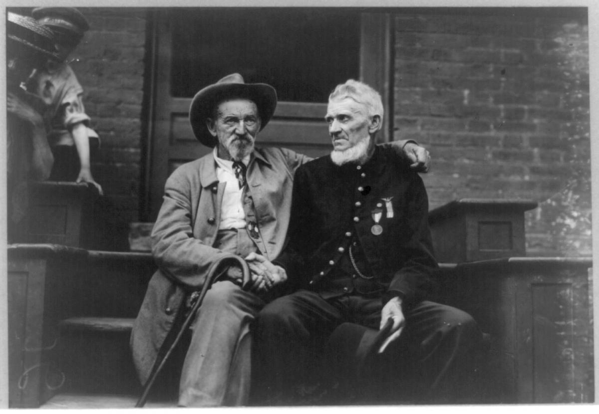 Two elderly men sit on a porch and shake hands