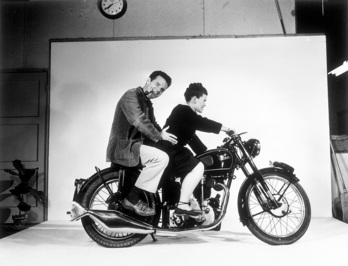 A woman and a man on a motorcycle in front of a film screen, as if they were shooting a picture.