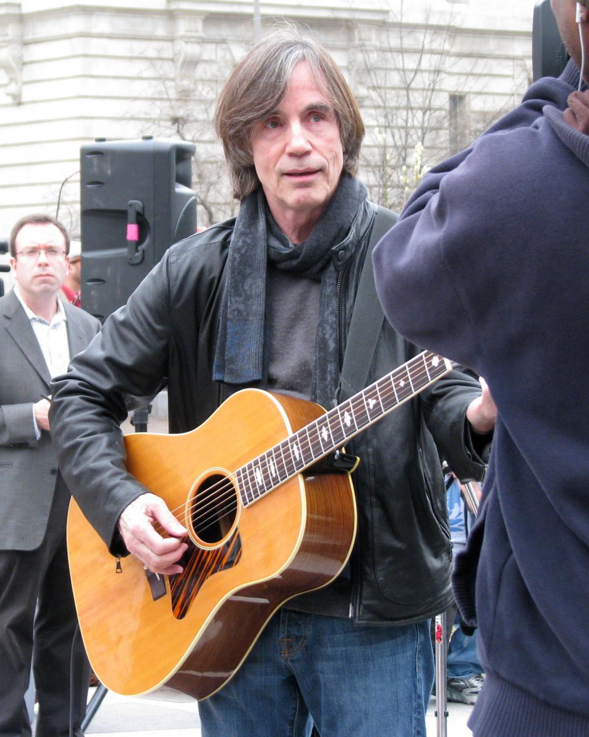 Color photo of a man in a leather jacket playing the guitar.