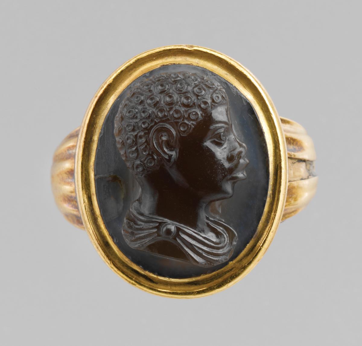 Gold frame with a black stone in the center, carved with the profile of a young African boy