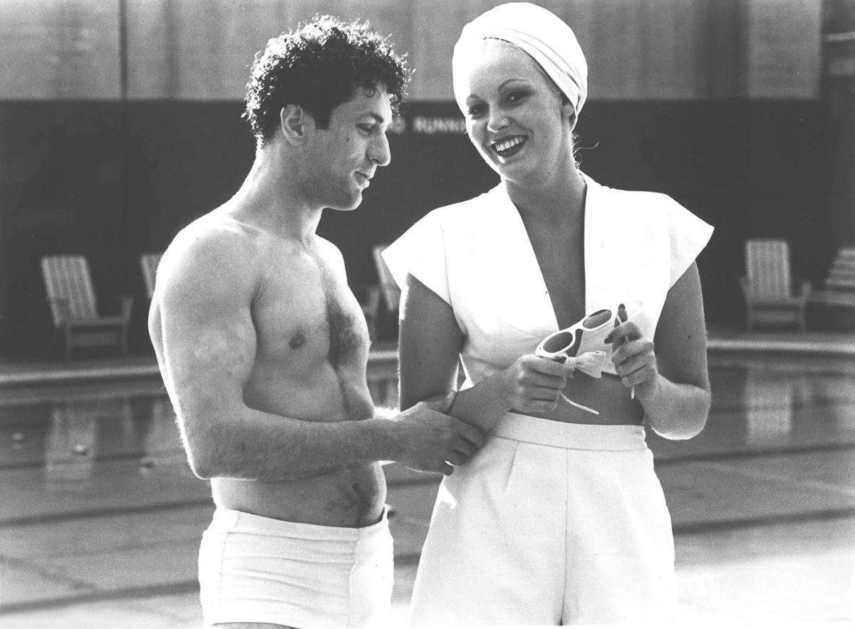 Shirtless Jake and Vicki, wearing a white swimsuit and bathing cap, talk, in this still from Raging Bull