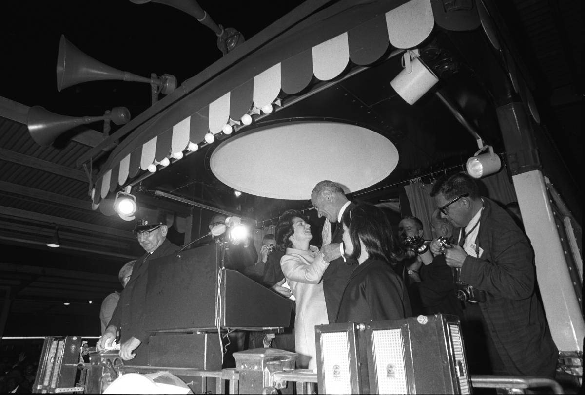 Black and white photo of Lady Bird Johnson embracing her husband behind a podium