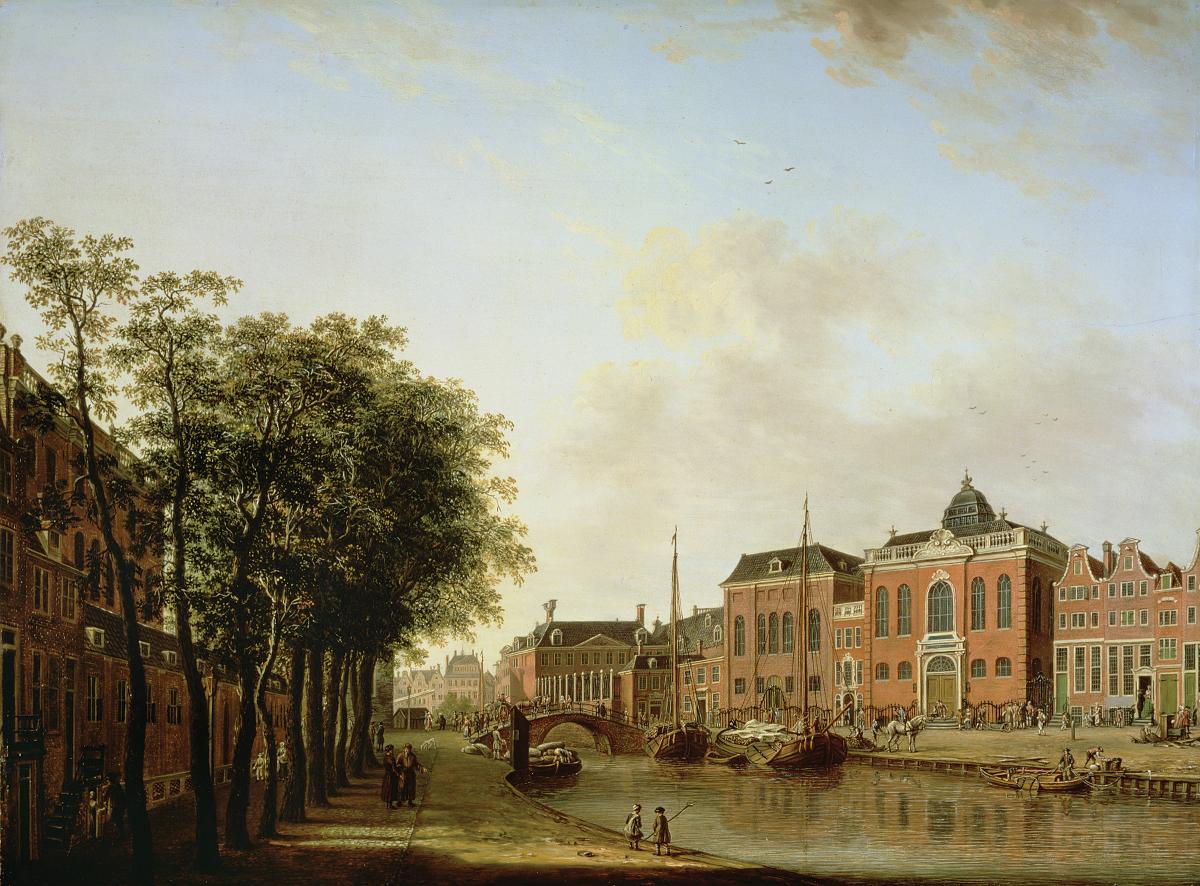 View of red brick buildings overlooking a canal, with a stand of trees on the left hand bank