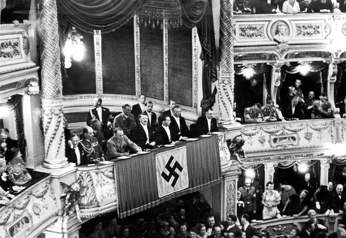 Black and white photo of the theatre box, hung with a nazi flag, in which Hitler sits with his party leaders at the Austrian opera