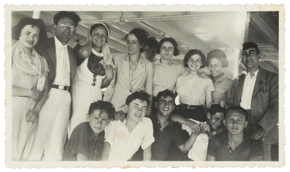 A group of young men and women pose, kneeling and standing in two rows, smiling, with their arms around each other