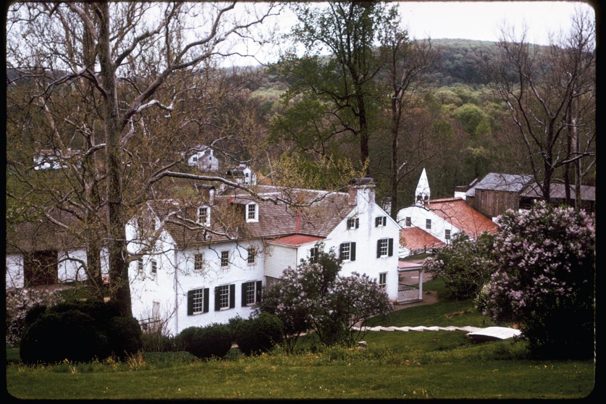 A view of Hopewell Furnace from a hill: white houses with brown roofs and chimneys, with a church to the far right