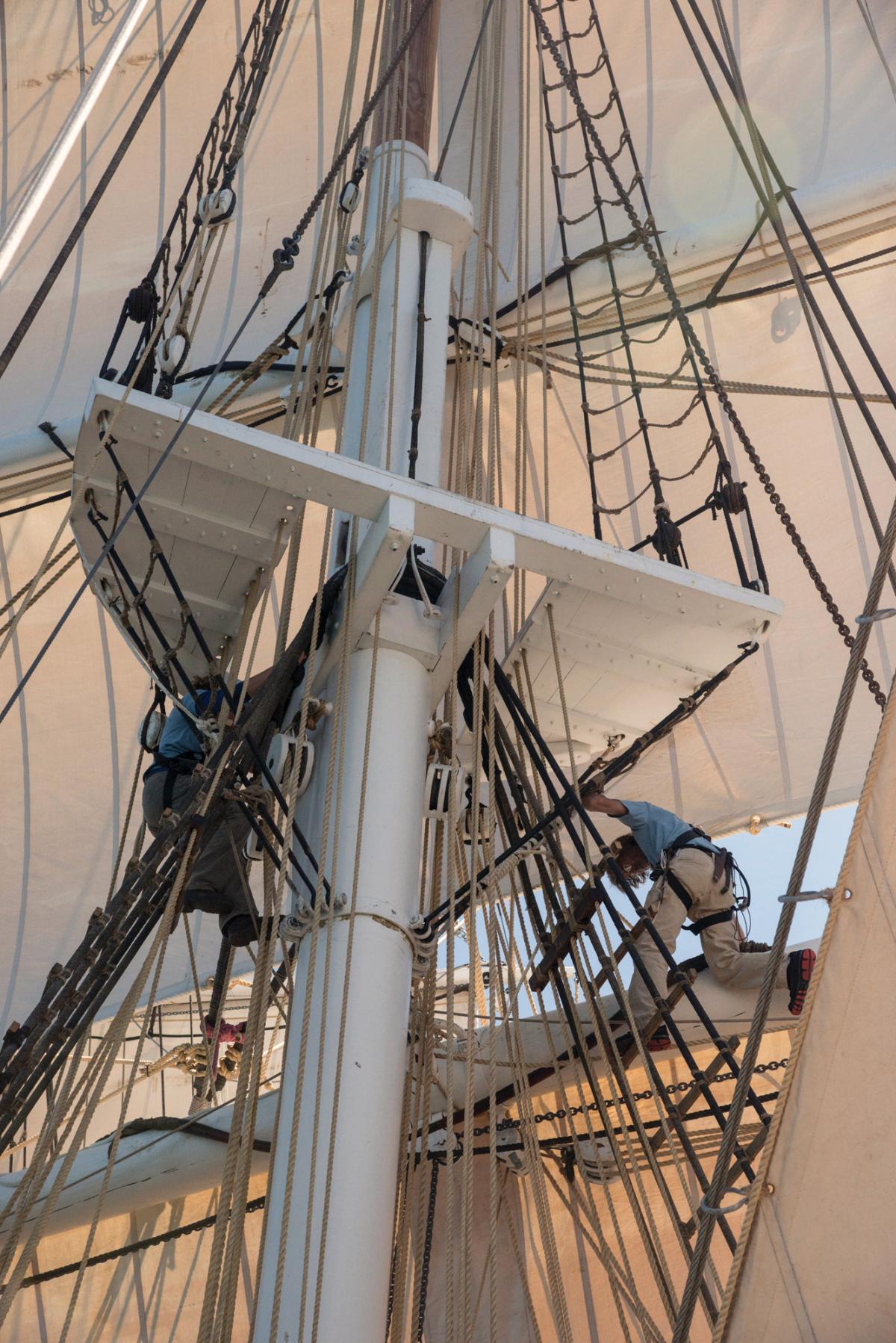 Deckhands climb up into the ropes of the rigging