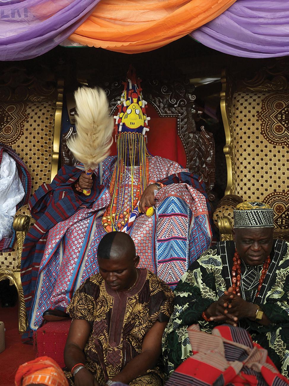 HRM Alayeluwa Oba Rufus Adeyemo Adejugbe Aladesanmi III, the Ewi of Ado-Ekiti, seated on a throne, holding a feathered fan, in traditional royal clothing
