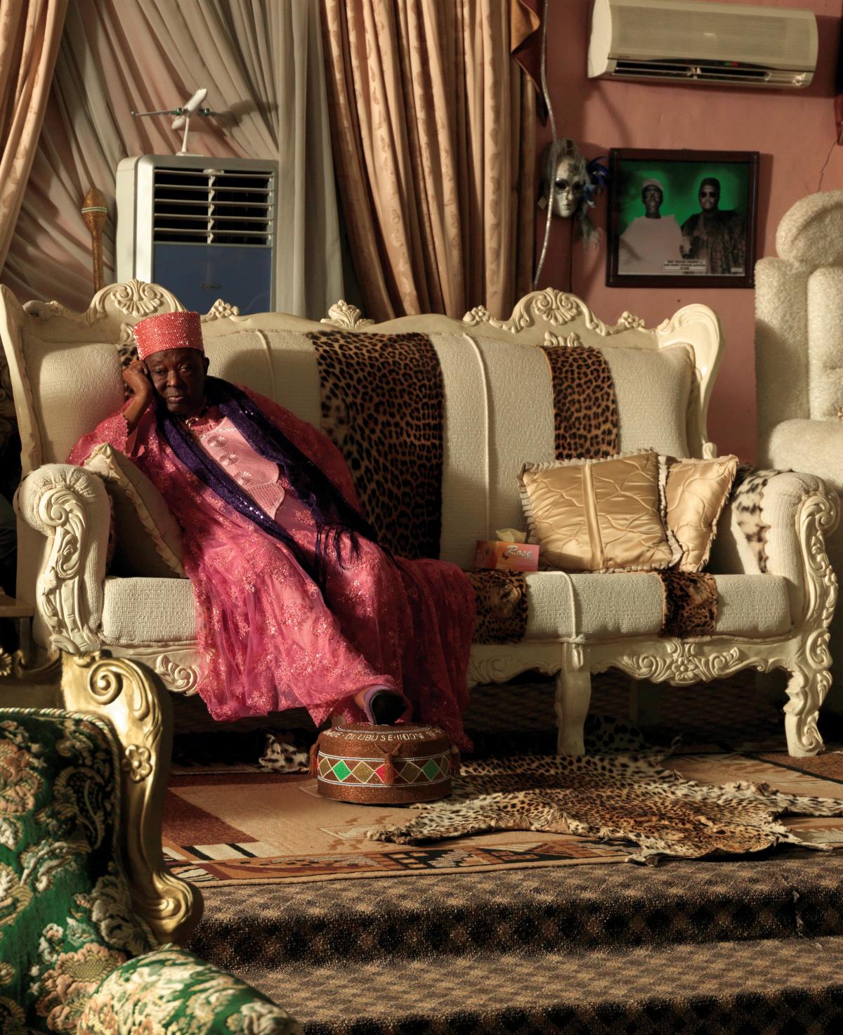 HRM Alayeluwa Oba Okunade Sijuwade, the Ooni of Ife, seated on a couch, wearing traditional, red robes, head resting on his hand