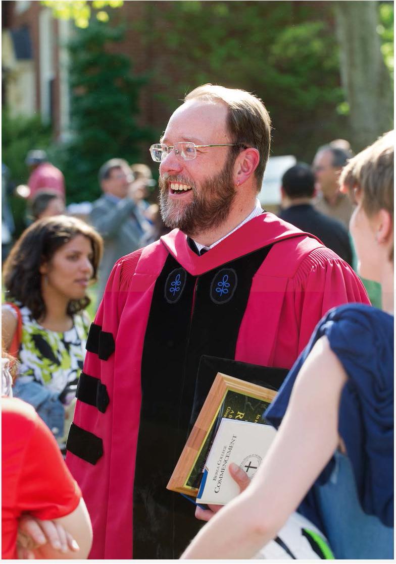 Professor Foster wearing commencement robes, walking down the graduation aisle