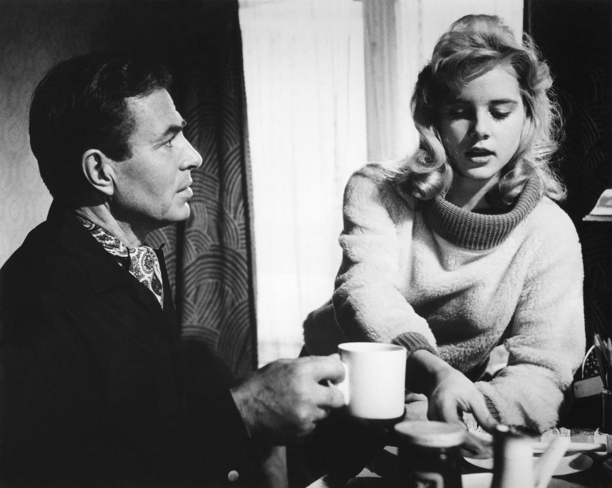 Black and white film still of a young girl and a man at a table