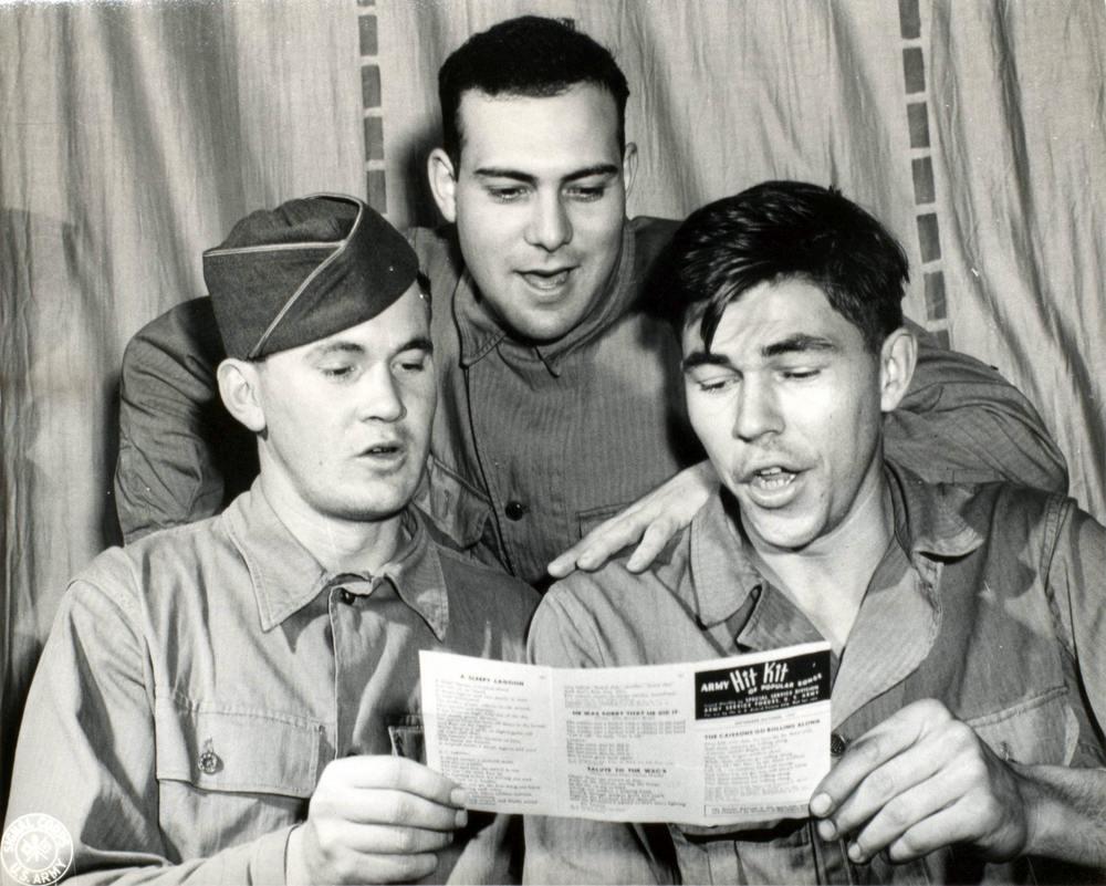 Three soldiers share a paper of the hit kit and sing along