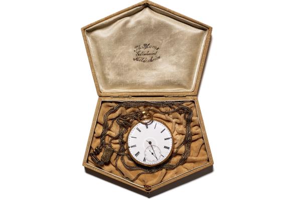 A pocket watch resting in a gold velvet pentagonal case