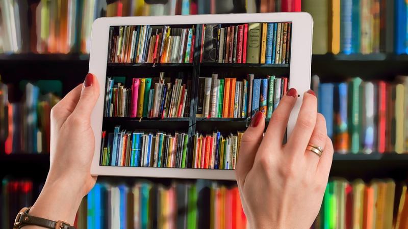 Two hands holding up a tablet in front of a large bookshelf