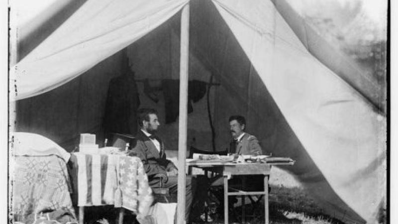 Black and white photo of Abraham Lincoln sitting with McClellan inside a general's tent.