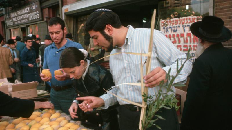 Jewish men and women look closely at produce at a sidewalk stand