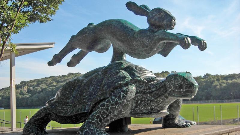 A brass hare leaps over a tortoise in a larger than life sculpture