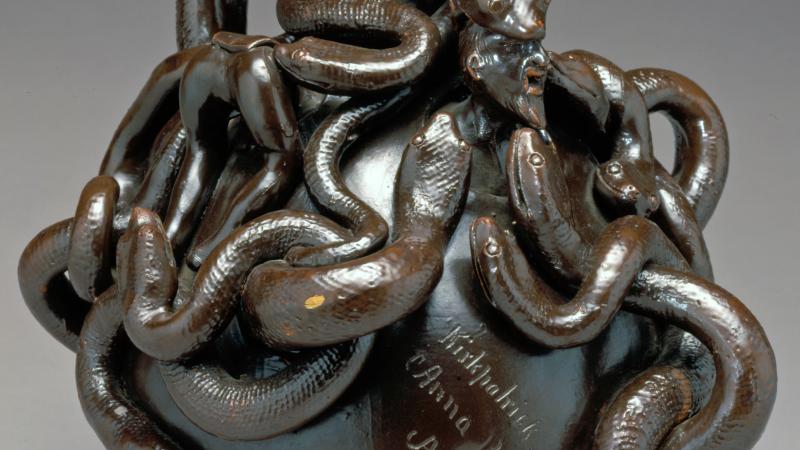 A twining mass of snakes twists around the top of a round jug with a narrow neck