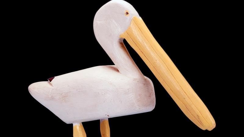 A white pelican with long yellow beak and feet, carved out of wood