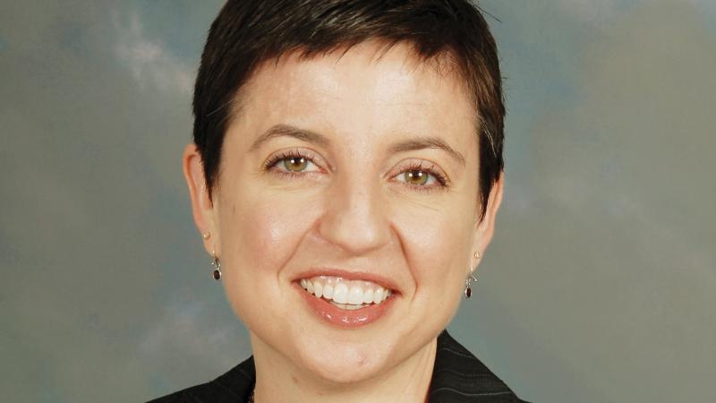 Fitzpatrick smiling, short dark hair, wearing a black blazer, maroon blouse and layered necklace with small maroon stones