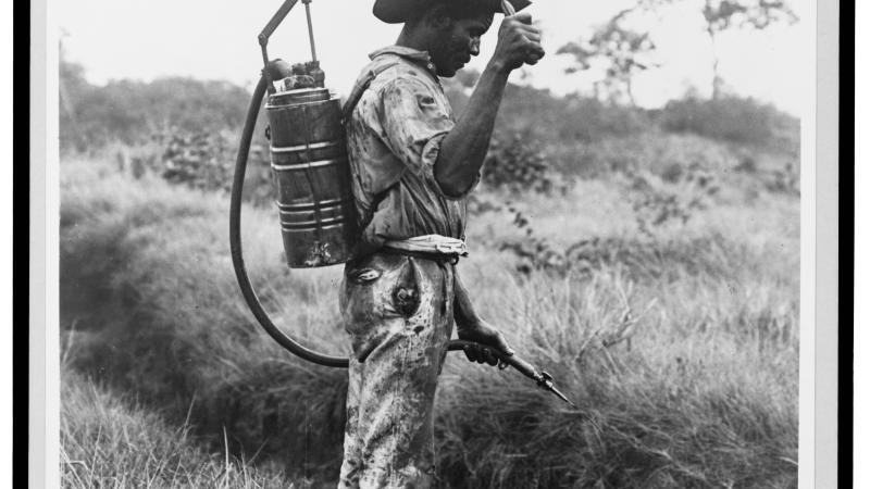 Black and white photo of a man spraying insecticide near the Panama Canal.
