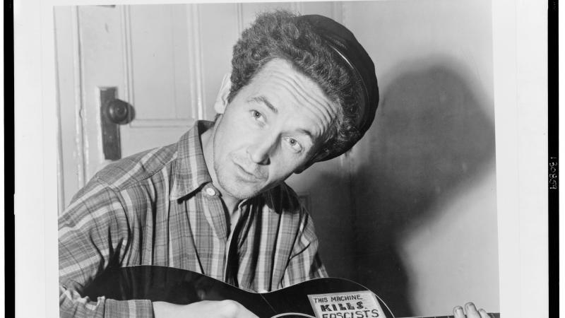 Guthrie in a plaid shirt, playing the guitar