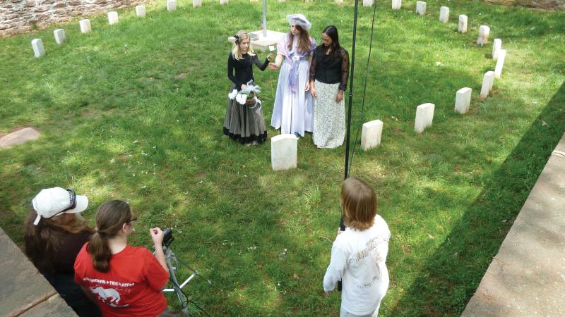 Photo of a group of young girls dressed in Civil War attire who are filmed in a small courtyard cemetery.
