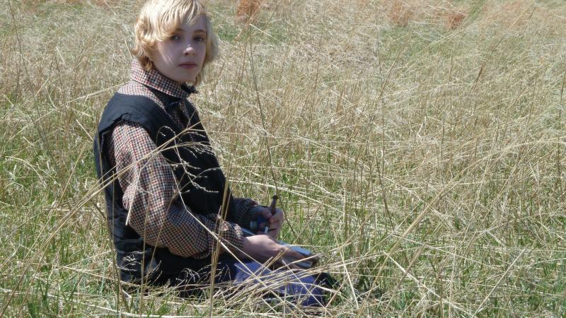 Photo of a young boy sitting in a field wearing a civilian outfit from the Civil War era.