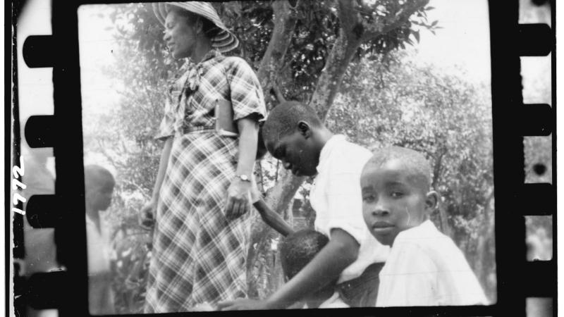 Black and white photo of a woman and three children under a shady tree.