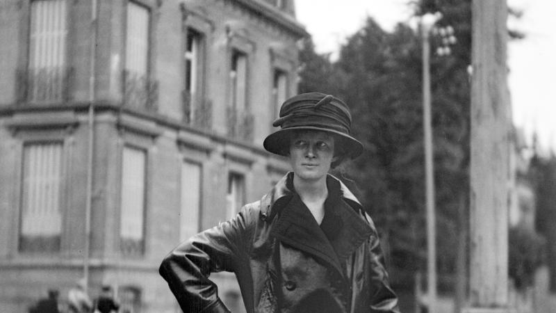 Black and white photo of a woman in an elegant raincoat and hat.