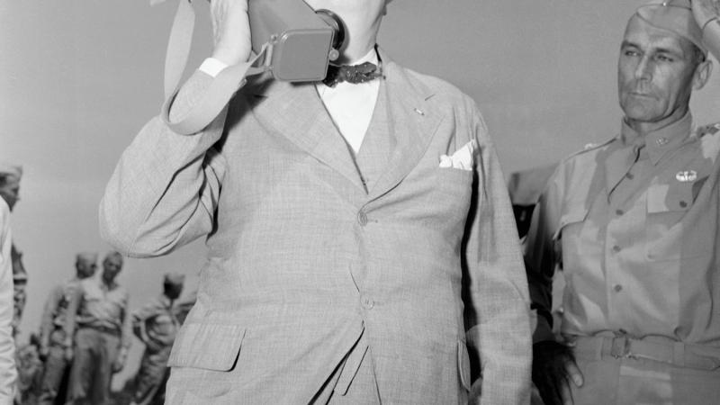 Black and white photo of Winston Churchill holding a large walkie-talkie to his ear.
