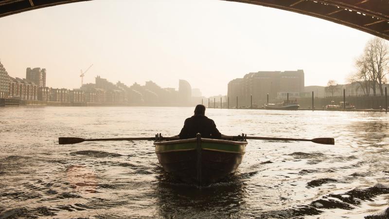 Silhouetted photo of Irons rowing a boat on the Thames, underneath a bridge